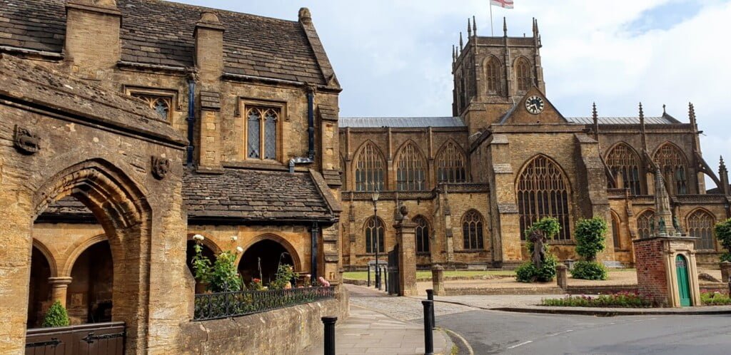 Sherborne abbey from the south west with the medieval almshouses in the foreground