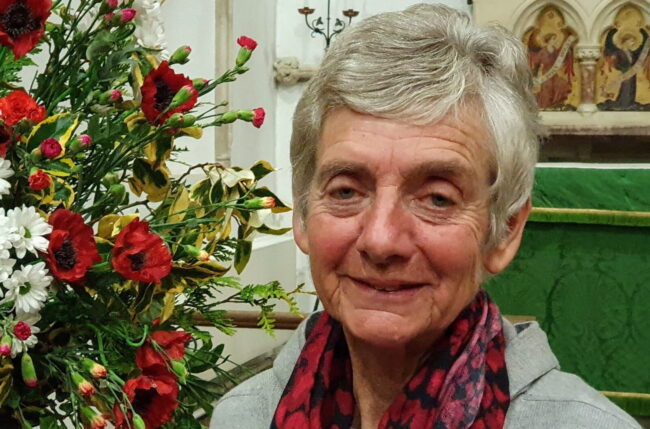 Photo of Pat Davidson - Guild President next to a flower arrangement in a church